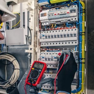 Man, an electrical technician working in a switchboard with fuses. Man, an electrical technician working in a switchboard with fuses. Installation and connection of electrical equipment. Professional uses a tablet.